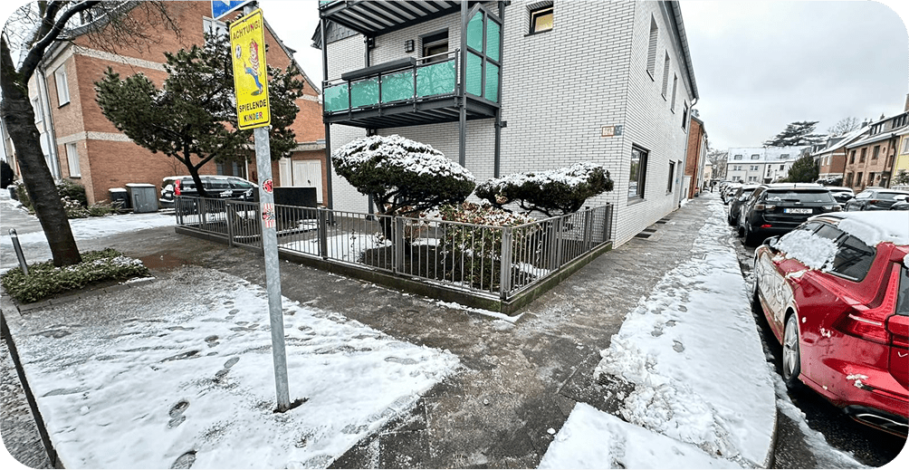 Geräumter Gehweg nach professionellem Winterdienst vor einem Mehrfamilienhaus.